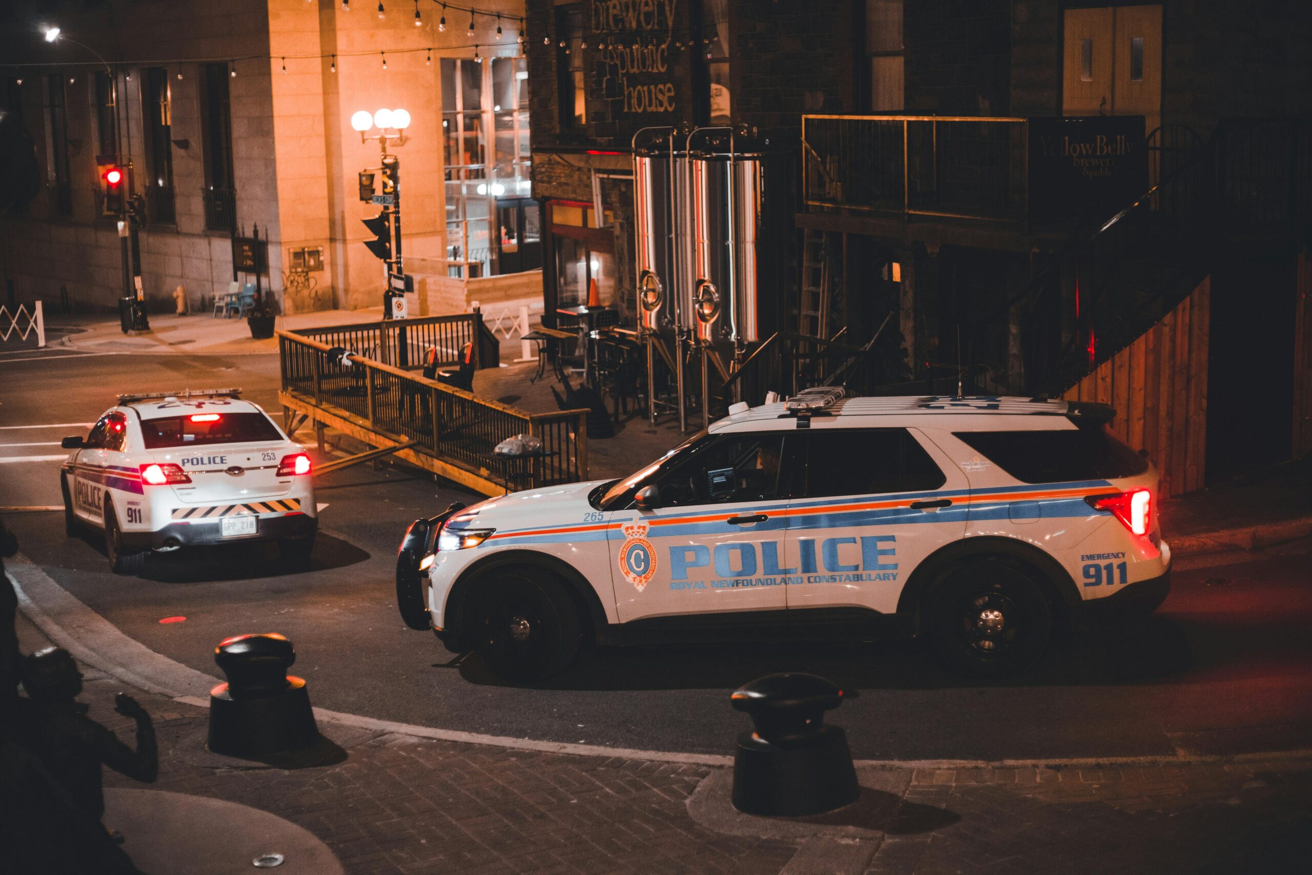 Two police cars patrolling a city street at night with warm lighting creating a dramatic urban mood.
