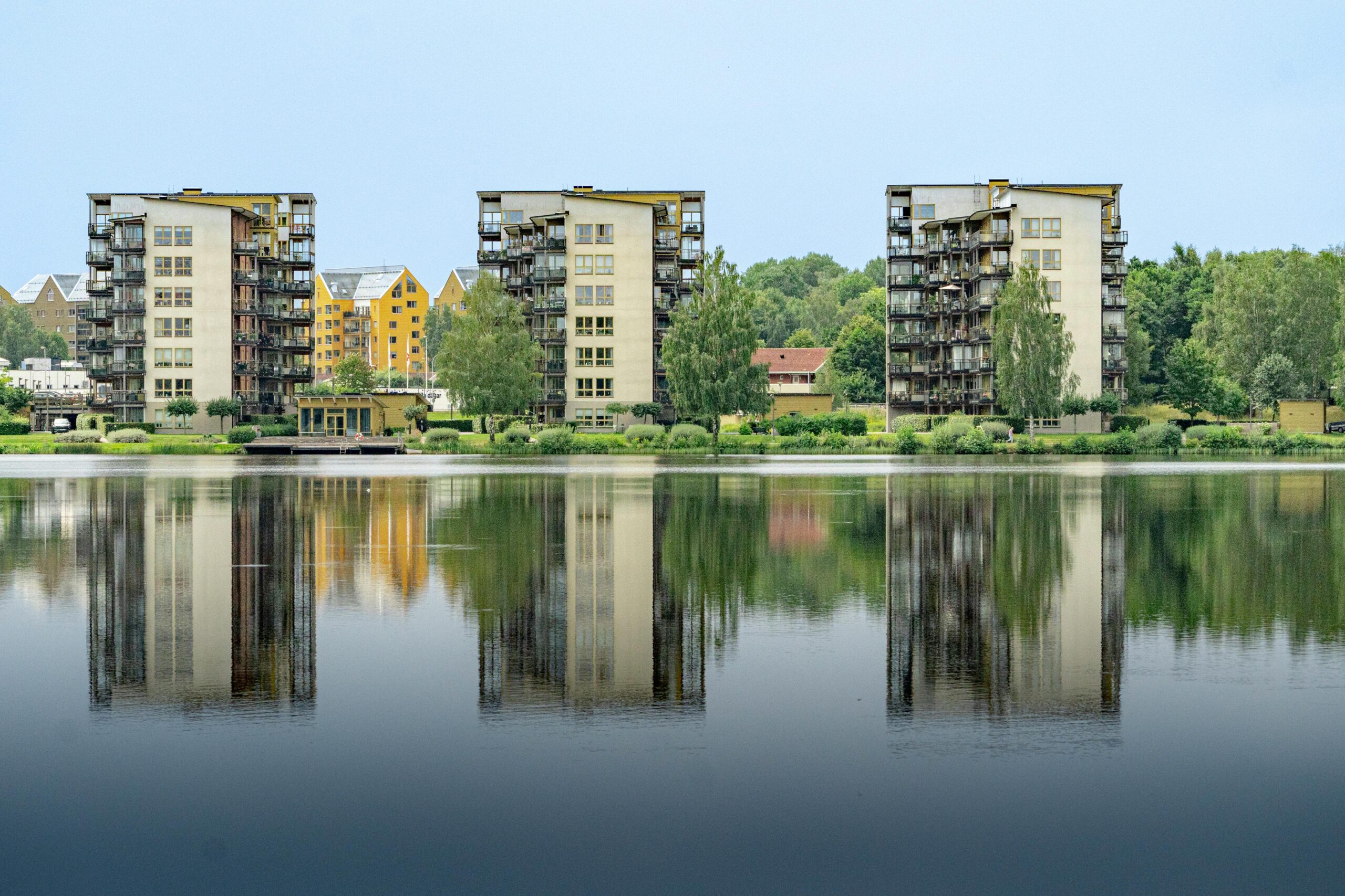 Reflection of modern residential buildings on a calm lake surrounded by lush greenery.