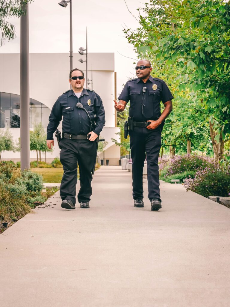 Two police officers walking down a pathway in a city park, engaged in conversation.