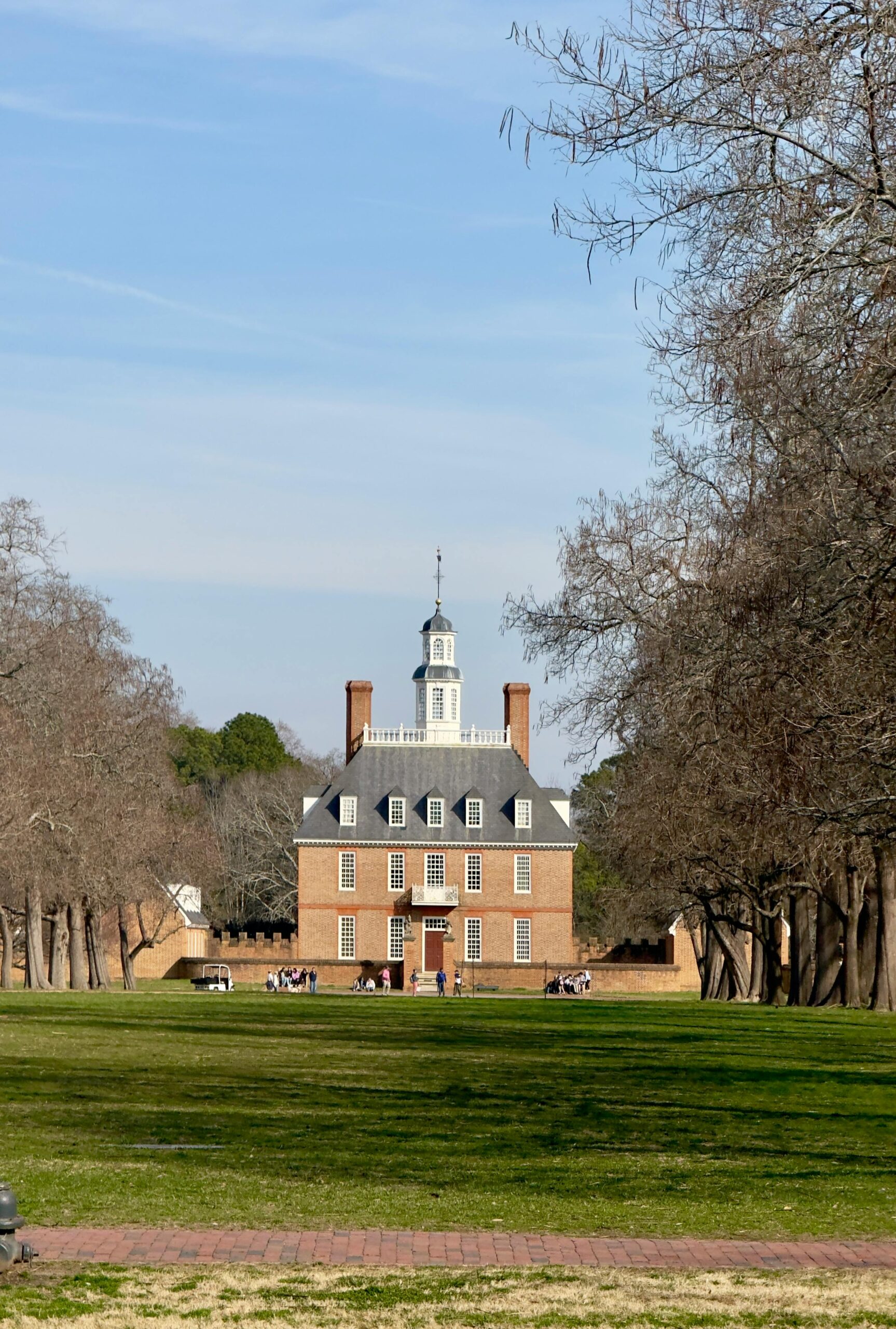 A view of the Governor's Palace in Colonial Williamsburg surrounded by trees and grass.